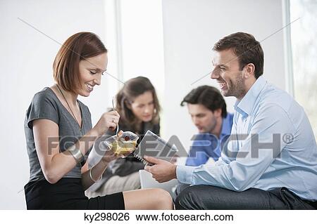 Woman eating food with their colleagues sitting with her View Large Photo Image Stock Photograph - Woman eating food with their colleagues sitting with her. Fotosearch