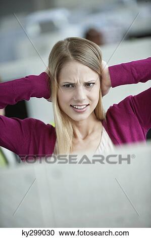 Stock Image - Businesswoman covering her ears in an office. Fotosearch