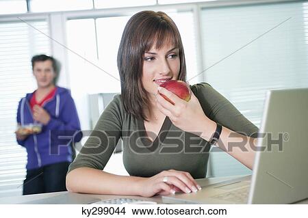 Businesswoman eating an apple and using a laptop View Large Photo Image Picture - Businesswoman eating an apple and using a laptop. Fotosearch