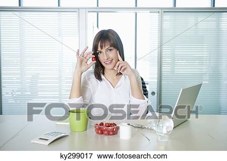 Stock Photo - Businesswoman holding a cherry tomato and smiling. Fotosearch