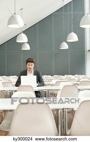 Businessman sitting at a cafeteria and using a laptop View Large Photo Image Picture - Businessman sitting at a cafeteria and using a laptop. Fotosearch