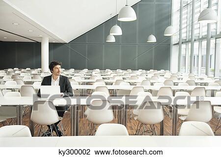 Businessman sitting at a cafeteria and using a laptop View Large Photo Image Stock Image - Businessman sitting at a cafeteria and using a laptop. Fotosearch
