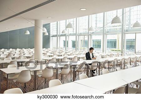 Businessman sitting at a cafeteria and using a laptop View Large Photo Image Stock Image - Businessman sitting at a cafeteria and using a laptop. Fotosearch
