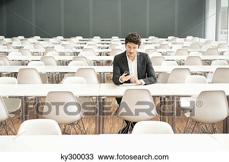 Businessman sitting at a cafeteria and using a mobile phone View Large Photo Image Stock Image - Businessman sitting at a cafeteria and using a mobile phone. Fotosearch