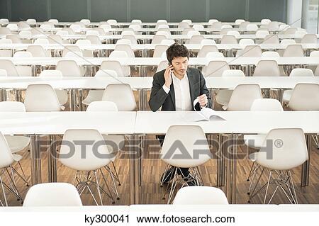 Businessman sitting at a cafeteria and talking on a mobile phone View Large Photo Image Stock Image - Businessman sitting at a cafeteria and talking on a mobile phone. Fotosearch