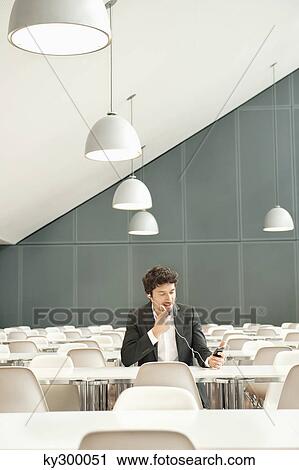 Businessman sitting at a cafeteria and talking on a mobile phone View Large Photo Image Stock Image - Businessman sitting at a cafeteria and talking on a mobile phone. Fotosearch