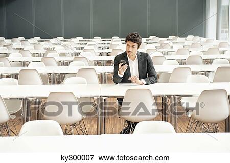 Businessman sitting at a cafeteria and using a mobile phone View Large Photo Image Stock Photo - Businessman sitting at a cafeteria and using a mobile phone. Fotosearch