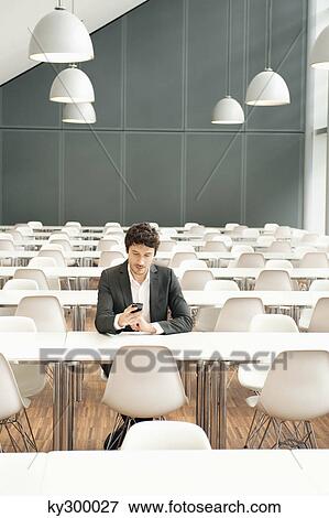 Businessman sitting at a cafeteria and using a mobile phone View Large Photo Image Stock Photo - Businessman sitting at a cafeteria and using a mobile phone. Fotosearch
