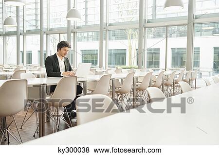 Stock Photo - Businessman sitting at a cafeteria and using a laptop. Fotosearch