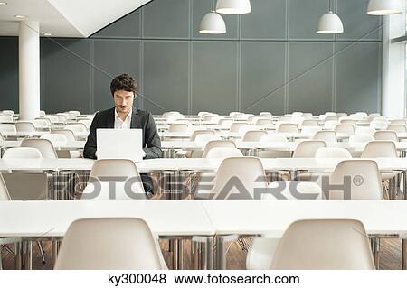 Businessman sitting at a cafeteria and using a laptop View Large Photo Image Stock Photo - Businessman sitting at a cafeteria and using a laptop. Fotosearch