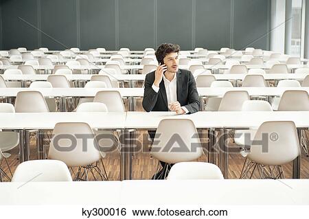Businessman sitting at a cafeteria and talking on a mobile phone View Large Photo Image Stock Photograph - Businessman sitting at a cafeteria and talking on a mobile phone. Fotosearch