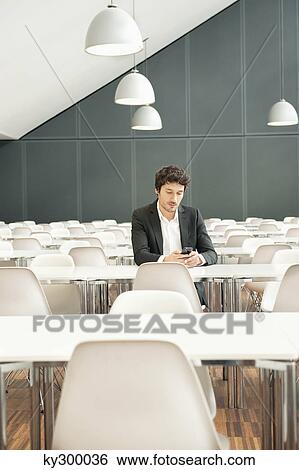Stock Photograph - Businessman sitting at a cafeteria and using a mobile phone. Fotosearch