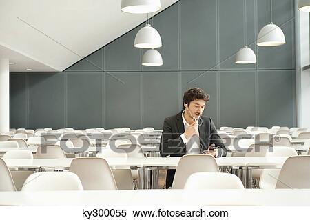 Businessman sitting at a cafeteria and talking on a mobile phone View Large Photo Image Stock Photography - Businessman sitting at a cafeteria and talking on a mobile phone. Fotosearch
