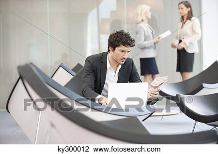 Stock Image - Businessman sitting in a waiting room and using a laptop. Fotosearch