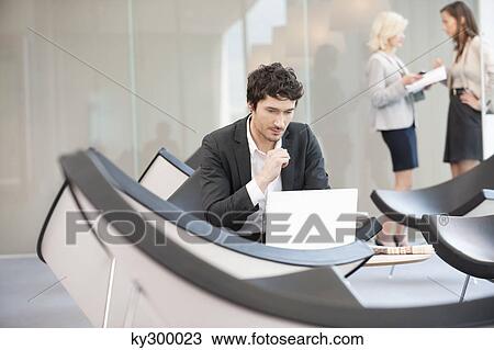 Businessman sitting in a waiting room and using a laptop View Large Photo Image Stock Image - Businessman sitting in a waiting room and using a laptop. Fotosearch