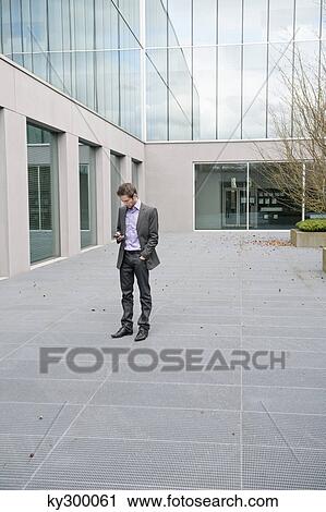 Stock Image - Businessman text messaging on a mobile phone. Fotosearch