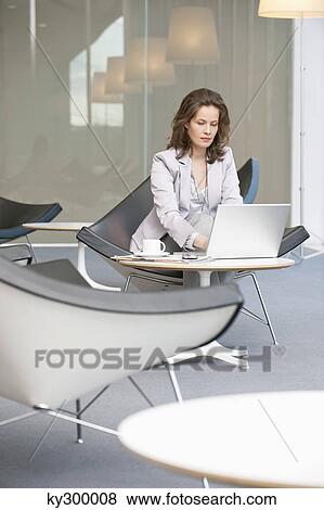 Businesswoman sitting on a chair and using a laptop View Large Photo Image Stock Photo - Businesswoman sitting on a chair and using a laptop. Fotosearch