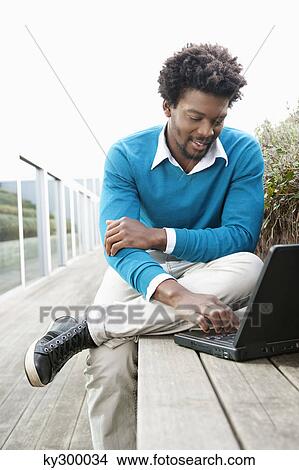 Picture - Man using a laptop on a boardwalk. Fotosearch