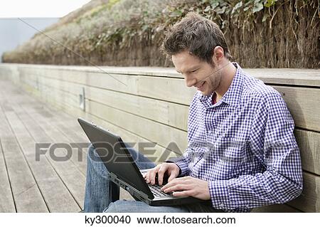 Man using a laptop on a boardwalk View Large Photo Image Stock Image - Man using a laptop on a boardwalk. Fotosearch