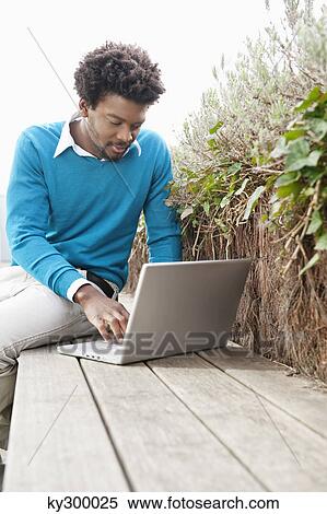 Man using a laptop on a boardwalk View Large Photo Image Stock Photography - Man using a laptop on a boardwalk. Fotosearch