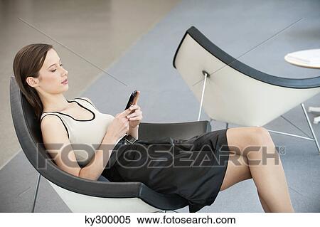Woman reclining in a chair and text messaging with a mobile phone View Large Photo Image Stock Photography - Woman reclining in a chair and text messaging with a mobile phone. Fotosearch
