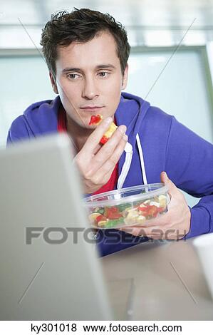 Businessman eating gum drops in front of a laptop View Large Photo Image Stock Photo - Businessman eating gum drops in front of a laptop. Fotosearch