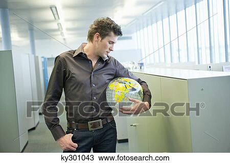 Businessman holding a globe and thinking in an office View Large Photo Image Stock Image - Businessman holding a globe and thinking in an office. Fotosearch