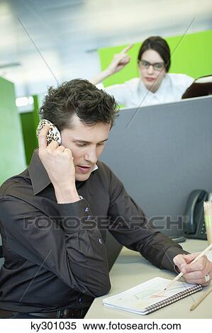 Businessmen talking on a mobile phone while his colleague looking angry View Large Photo Image Stock Photography - Businessmen talking on a mobile phone while his colleague looking angry. Fotosearch