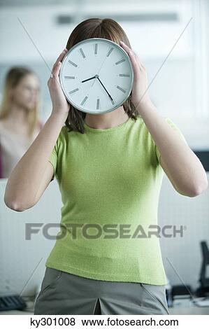 Stock Photo - Businesswoman holding a clock in front of her face. Fotosearch