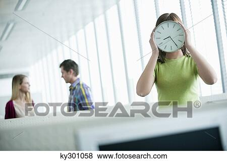 Businesswoman holding a clock in front of her face View Large Photo Image Stock Photo - Businesswoman holding a clock in front of her face. Fotosearch