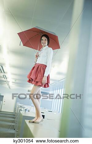 Businesswoman holding an umbrella and standing on a desk in an office View Large Photo Image Picture - Businesswoman holding an umbrella and standing on a desk in an office. Fotosearch