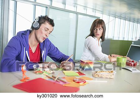 Businesswoman looking at a businessman listening to headphones and writing View Large Photo Image Stock Image - Businesswoman looking at a businessman listening to headphones and writing. Fotosearch