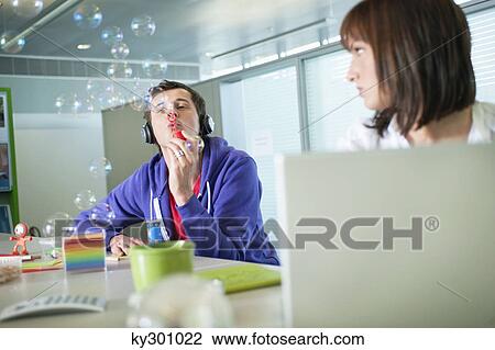 Businesswoman looking at a businessman listening to headphones and blowing bubbles View Large Photo Image Stock Image - Businesswoman looking at a businessman listening to headphones and blowing bubbles. Fotosearch