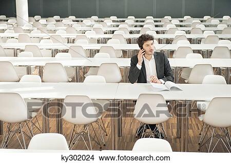 Businessman sitting at a cafeteria and talking on a mobile phone View Large Photo Image Picture - Businessman sitting at a cafeteria and talking on a mobile phone. Fotosearch