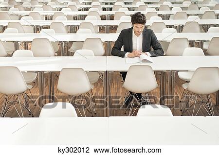 Stock Image - Businessman sitting at a cafeteria and reading a book. Fotosearch