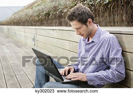 Stock Image - Man using a laptop on a boardwalk. Fotosearch