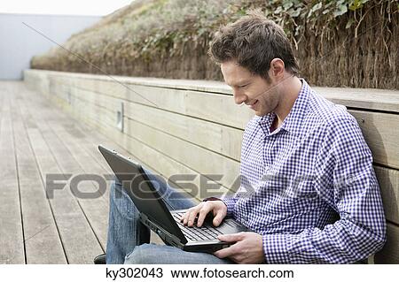 Man using a laptop on a boardwalk View Large Photo Image Stock Image - Man using a laptop on a boardwalk. Fotosearch