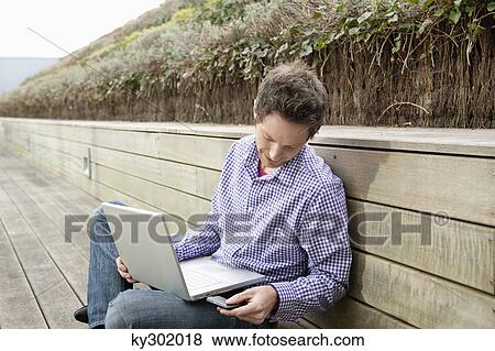 Stock Photo - Man using a laptop on a boardwalk. Fotosearch
