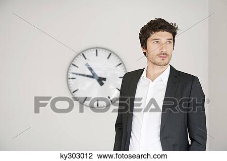 Businessman standing in front of a clock View Large Photo Image Stock Image - Businessman standing in front of a clock. Fotosearch