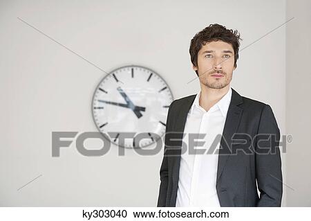 Businessman standing in front of a clock View Large Photo Image Stock Image - Businessman standing in front of a clock. Fotosearch