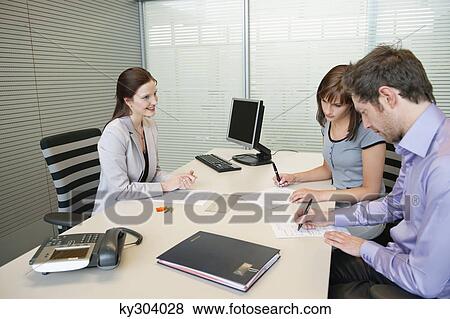 Couple signing agreement form in a real estate agent's office View Large Photo Image Stock Photo - Couple signing agreement form in a real estate agent's office. Fotosearch