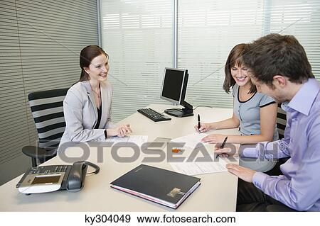 Couple signing agreement form in a real estate agent's office View Large Photo Image Stock Photo - Couple signing agreement form in a real estate agent's office. Fotosearch