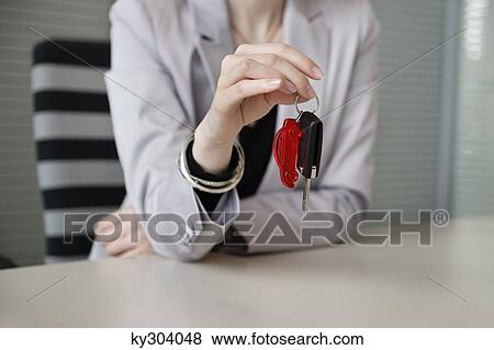 Stock Photo - Female financial advisor holding a car key in an office. Fotosearch