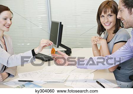 Stock Image - Female real estate agent giving house keys to a couple. Fotosearch