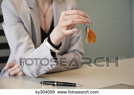 Female real estate agent holding house keys in an office View Large Photo Image Stock Photo - Female real estate agent holding house keys in an office. Fotosearch