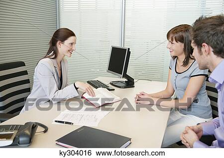 Stock Photograph - Female real estate agent showing a book to a couple. Fotosearch