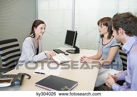 Stock Photograph - Female real estate agent showing a book to a couple. Fotosearch