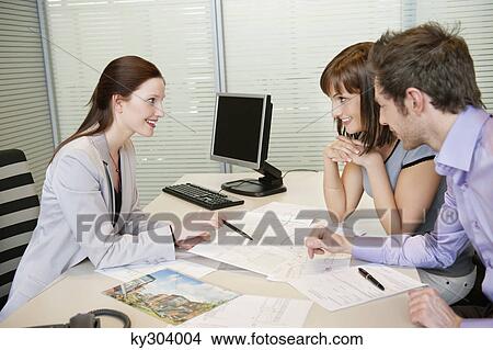 Female real estate agent showing a brochure to a couple View Large Photo Image Picture - Female real estate agent showing a brochure to a couple. Fotosearch