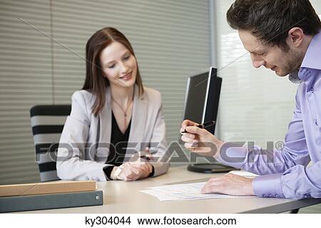 Picture - Man signing documents with a female real estate agent sitting in front of him. Fotosearch