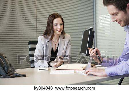 Stock Image - Man signing documents with a female real estate agent sitting in front of him. Fotosearch